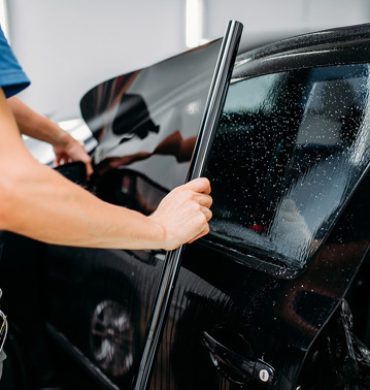 Male specialist applying car tinting film, installation process, tinted auto glass installing procedure